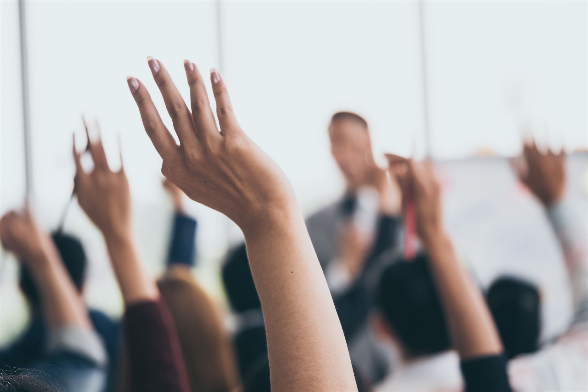 Close-up-of-raised-hands-at-office-training-with-speaker-out-of-focus-in-background